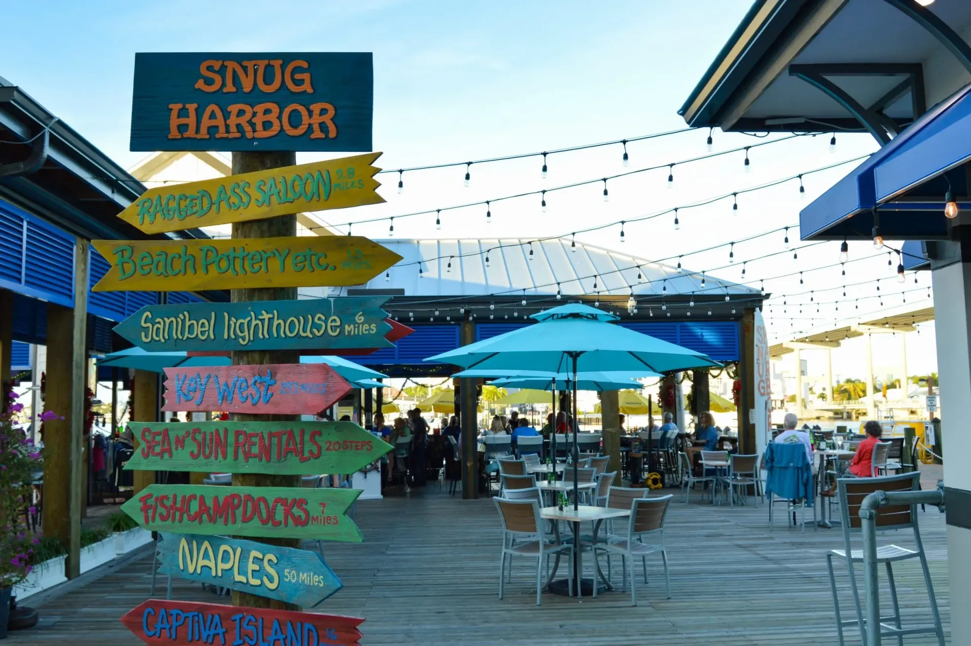 A restaurant with tables and umbrellas and a sign that says snug harbor