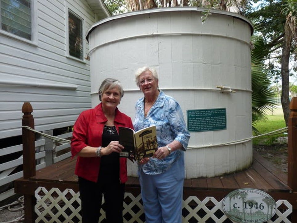Two women standing in front of a large white tank that says c. 1936