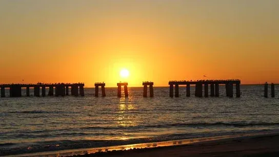 The sun is setting over a pier in the ocean.