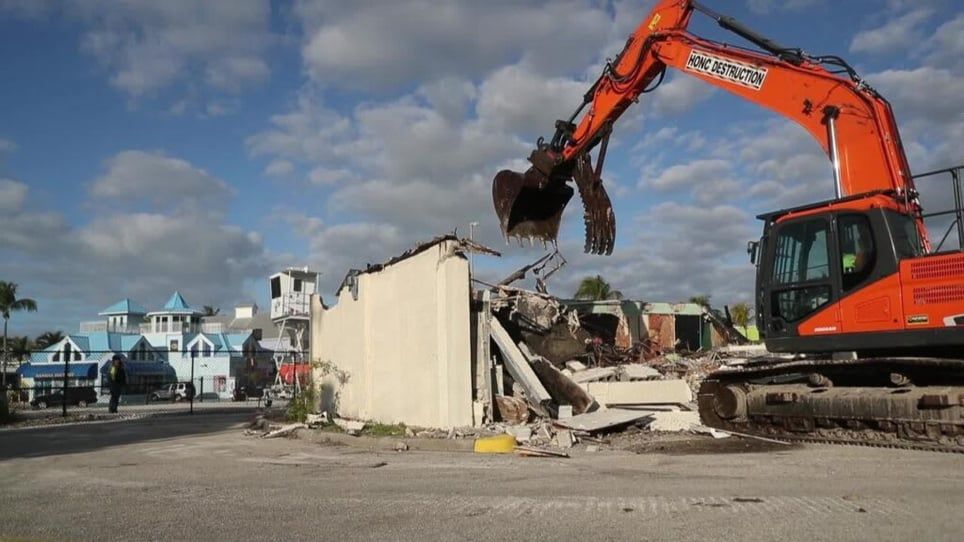 A large orange excavator is demolishing a building.
