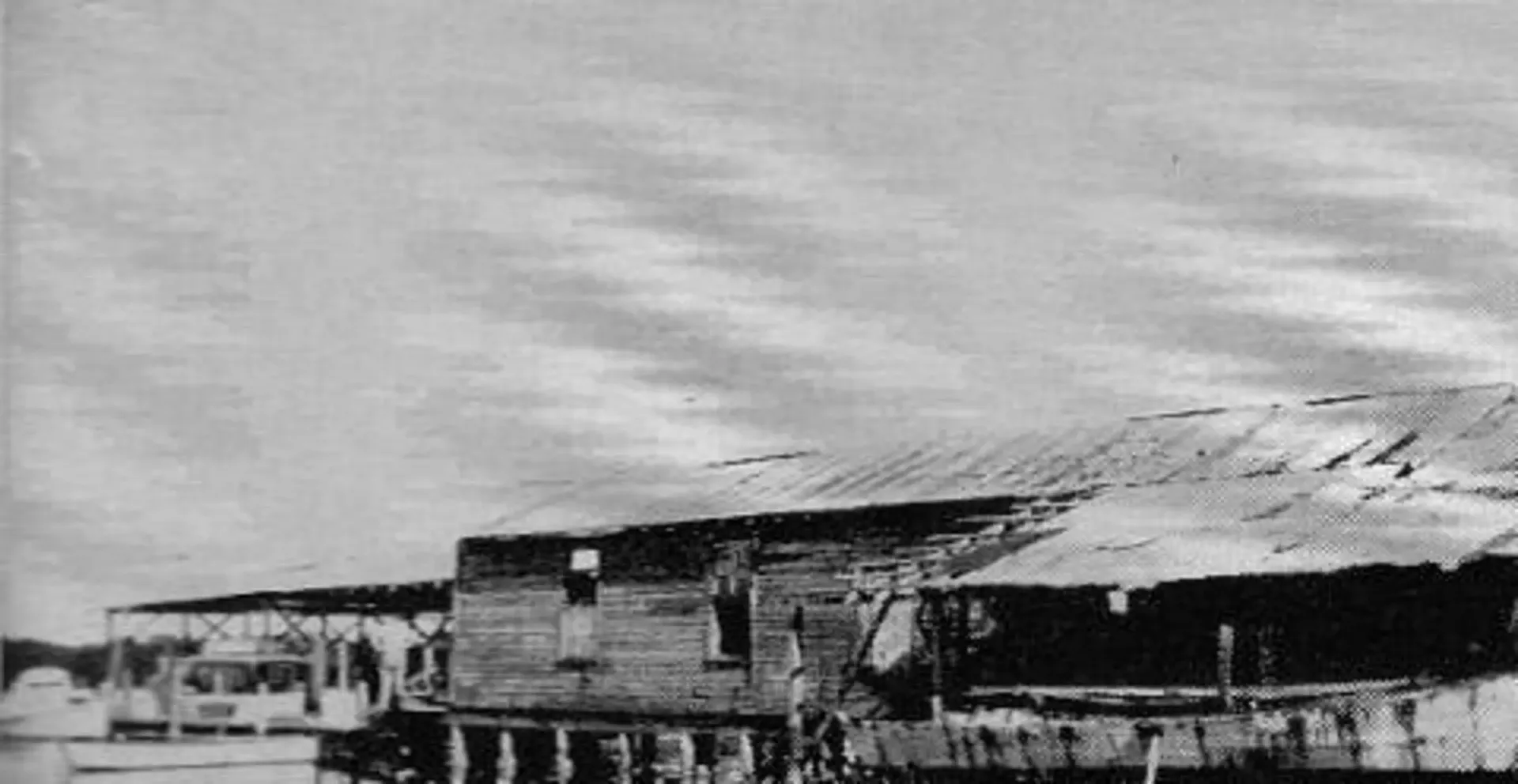 A black and white photo of a house with a cloudy sky in the background.