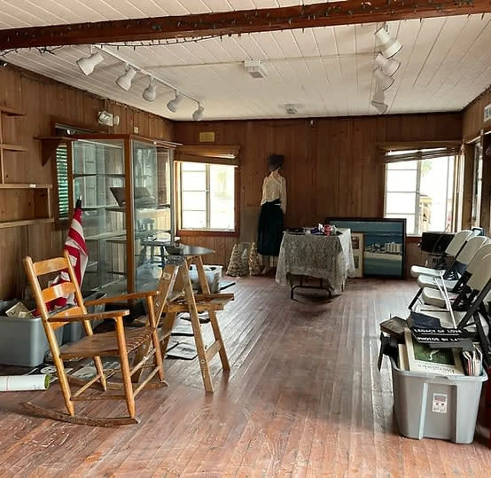 A room with wooden walls , chairs , a table and a display case.