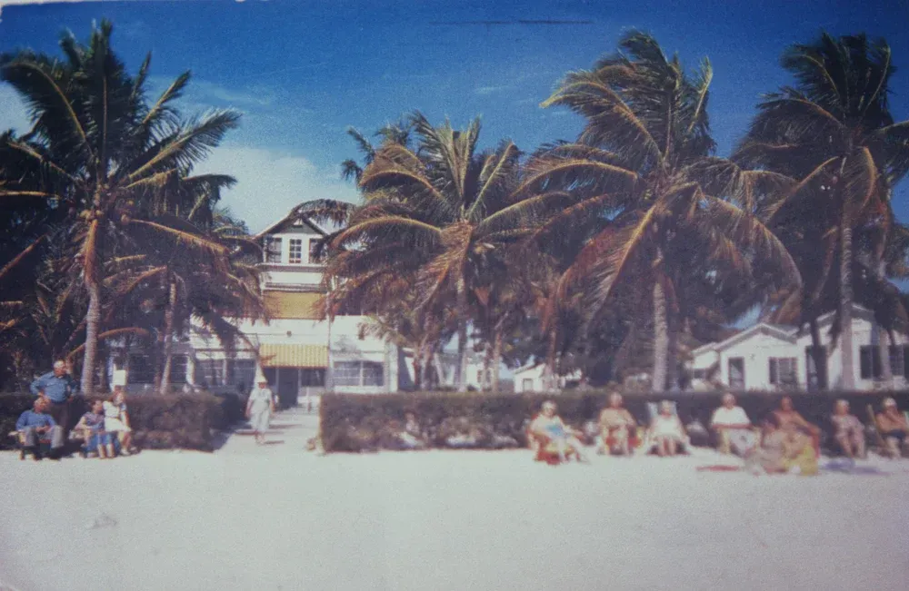 A group of people are sitting on the beach in front of a house