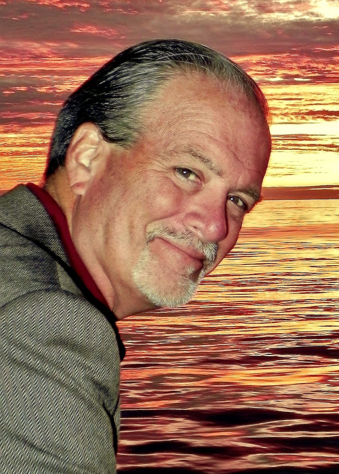 Man smiling at sunset with calm ocean and golden-red sky in the background