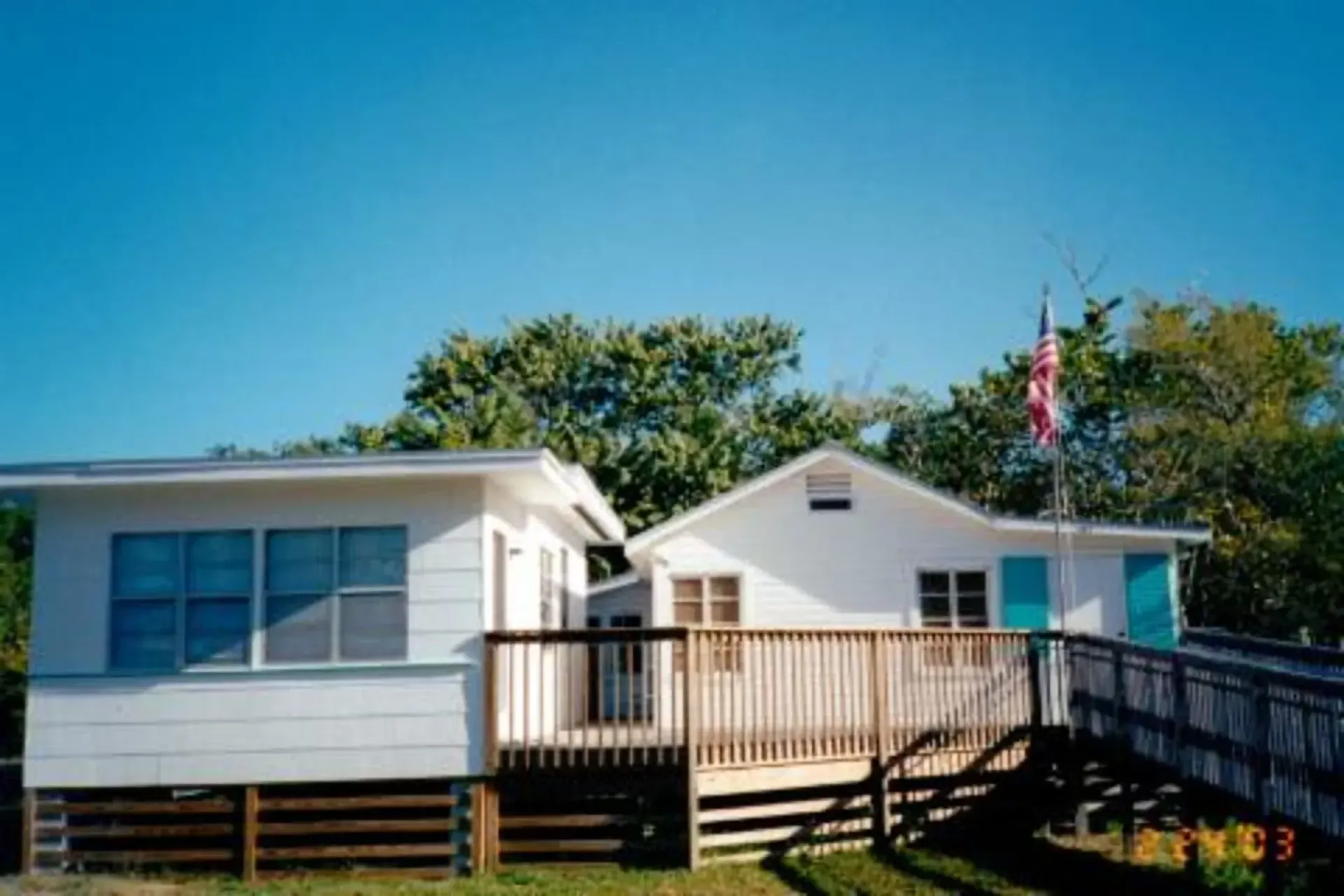 A white house with a wooden deck and an american flag on top