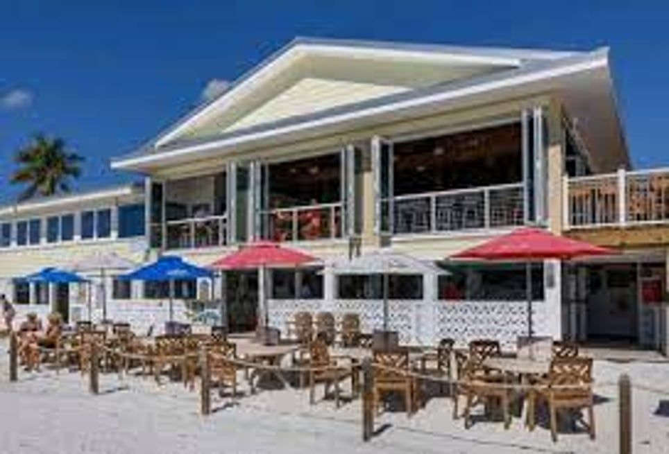 A large building with tables and chairs on the beach in front of it.