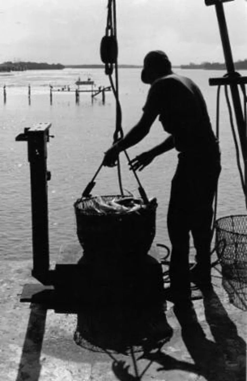 A black and white photo of a man cooking food on a boat