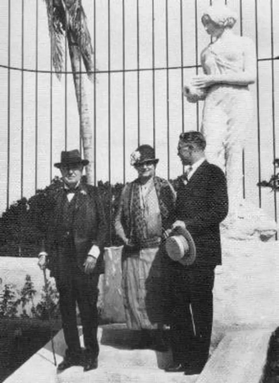A black and white photo of three men standing in front of a statue