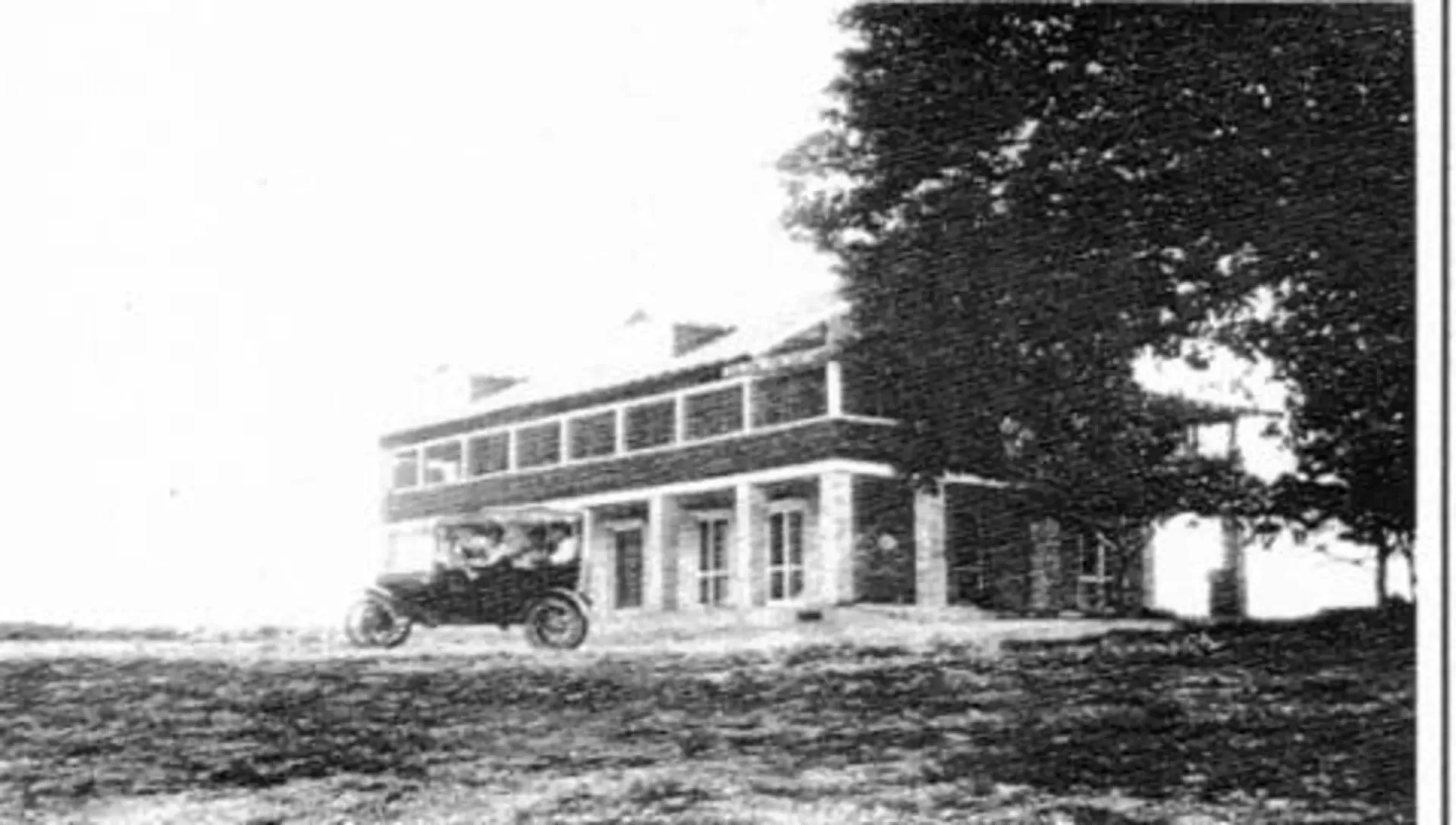 A black and white photo of a house with a car parked in front of it.