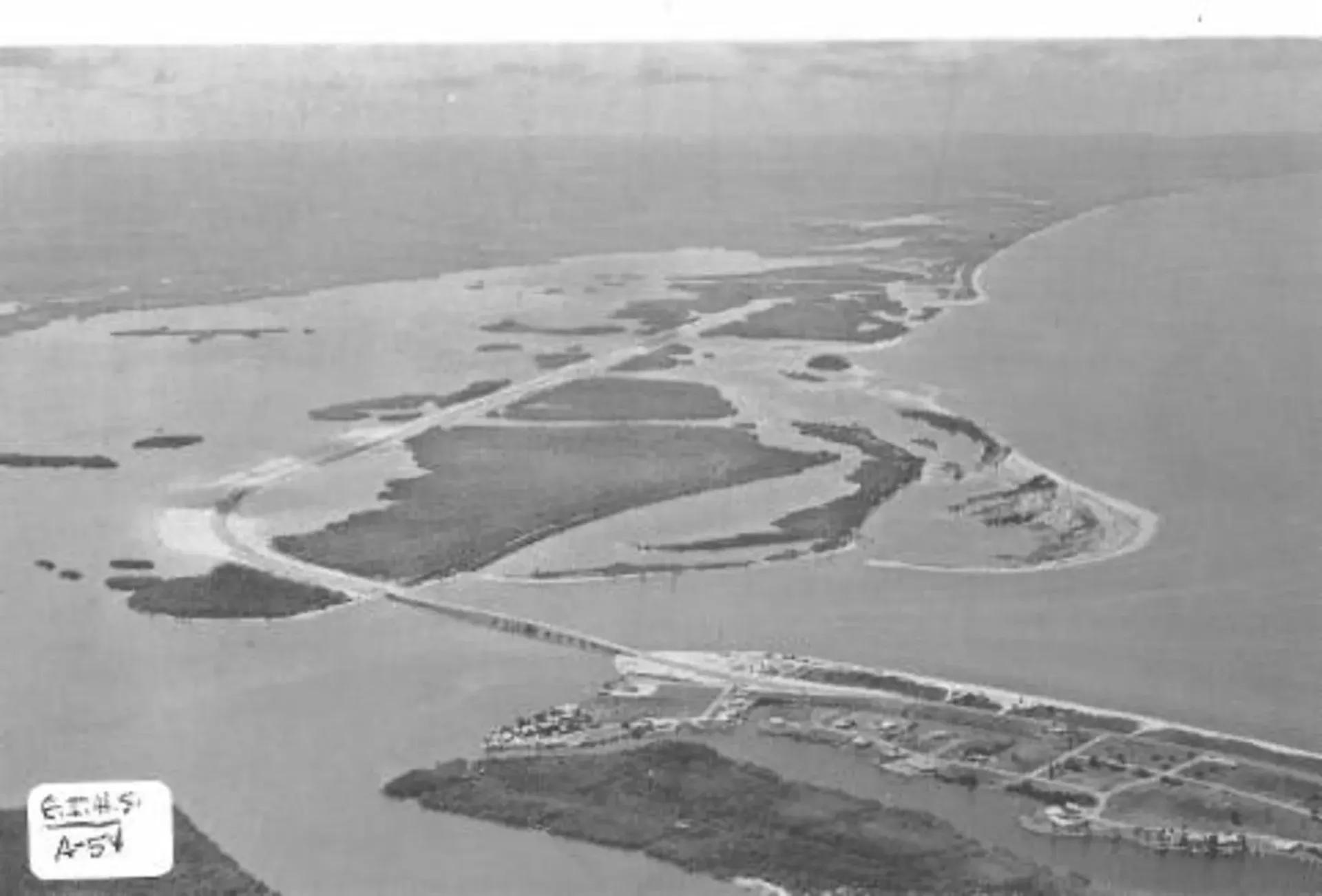 Aerial view of a coastal island or sandbar surrounded by water, with boats near shore.