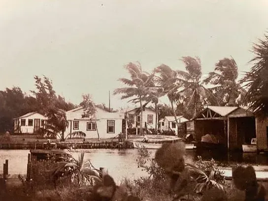 A black and white photo of a house next to a body of water.