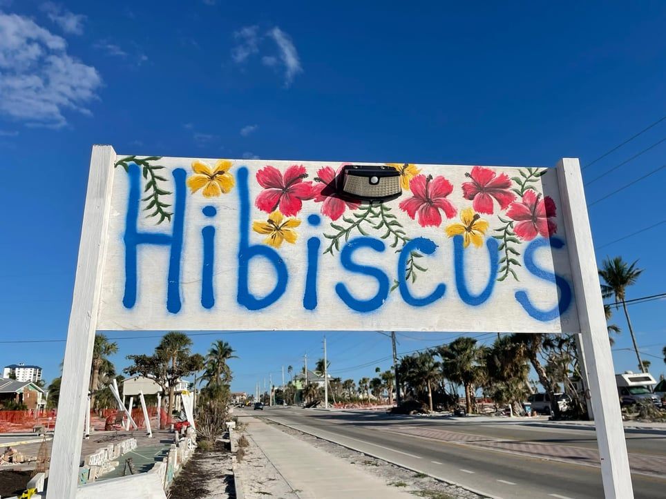 A sign that says hibiscus with flowers painted on it