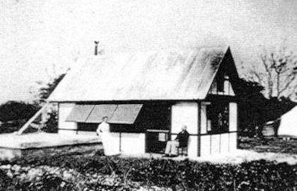 A black and white photo of a small house with a tin roof.