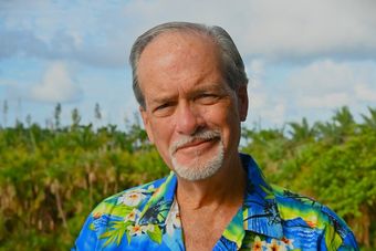 Smiling man in a gray jacket against a vivid sunset over water