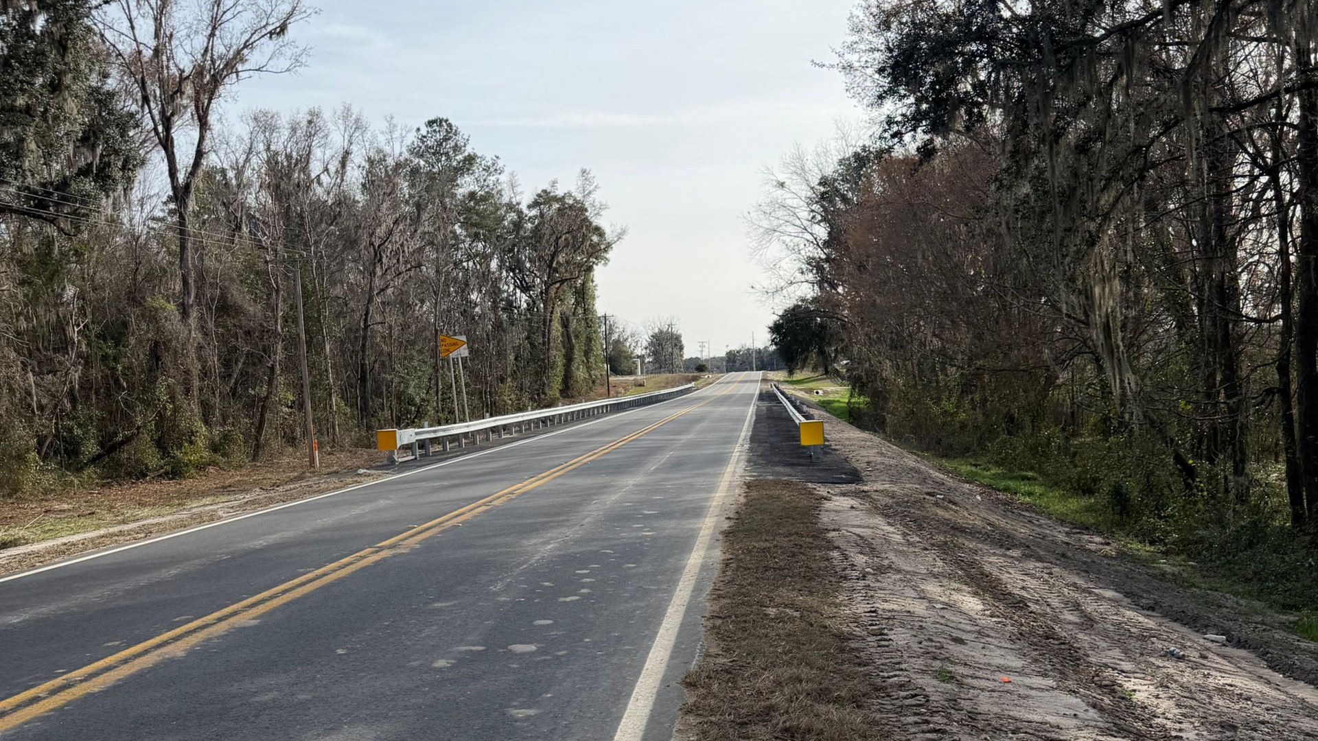 Empty rural road with yellow center lines, trees on both sides, and a partly cloudy sky