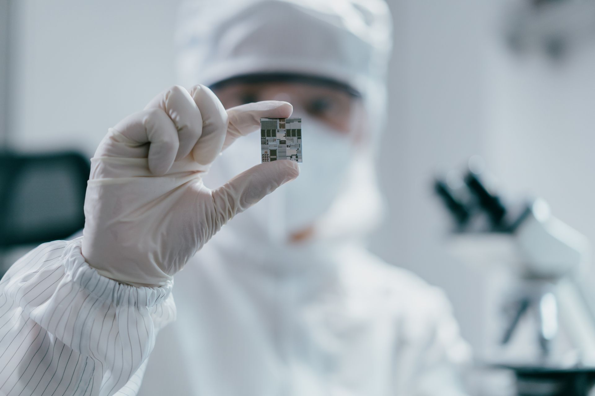 A scientist in a clean room is holding a small object in his hand.