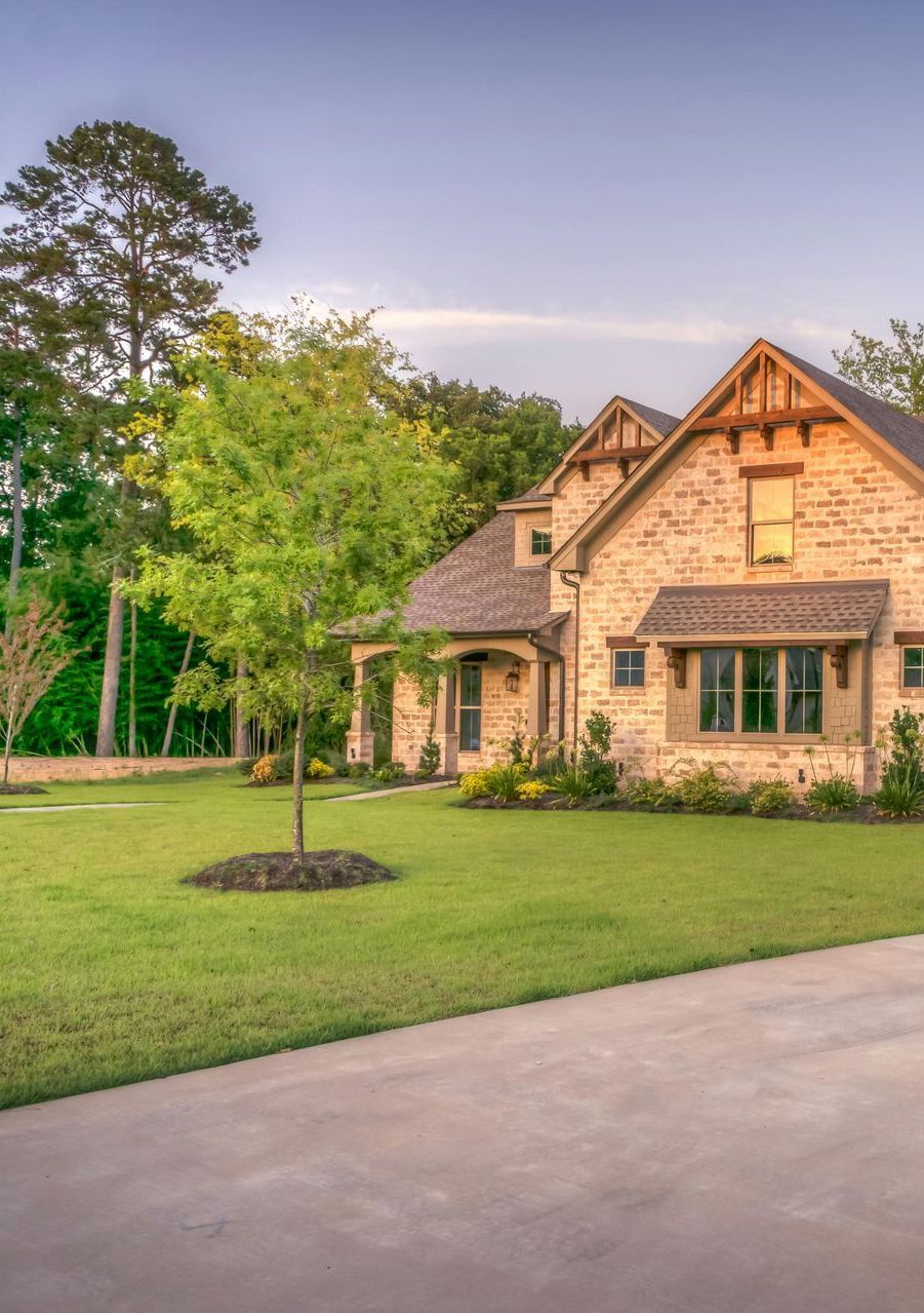 A large brick house with a driveway and a tree in front of it.