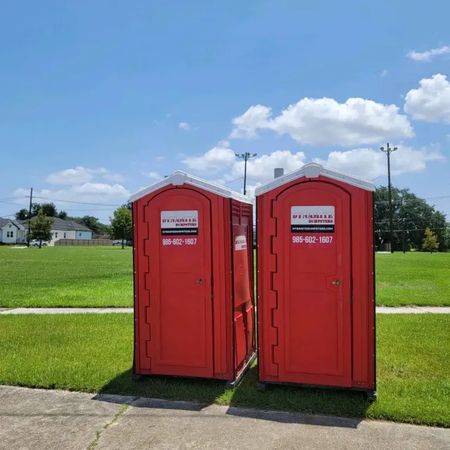 Two red portable toilets are sitting next to each other in a grassy field.