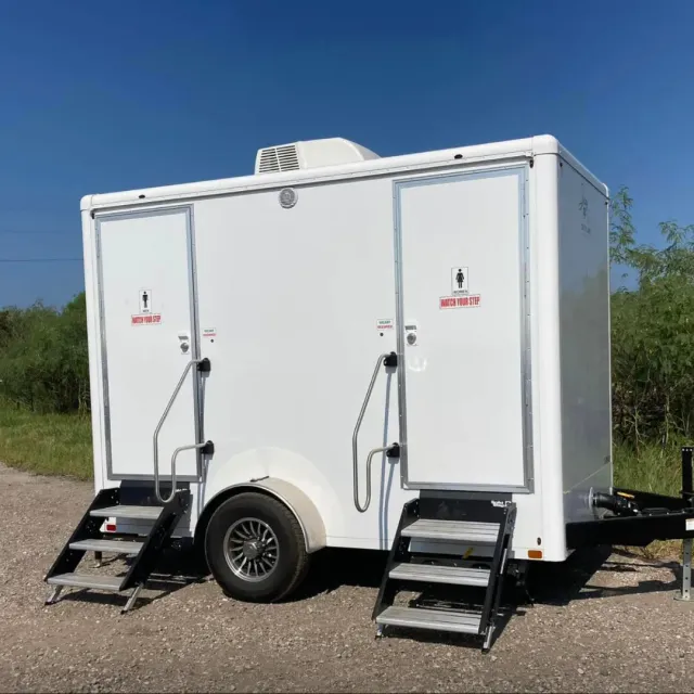 A white trailer with stairs attached to it is parked on the side of the road.