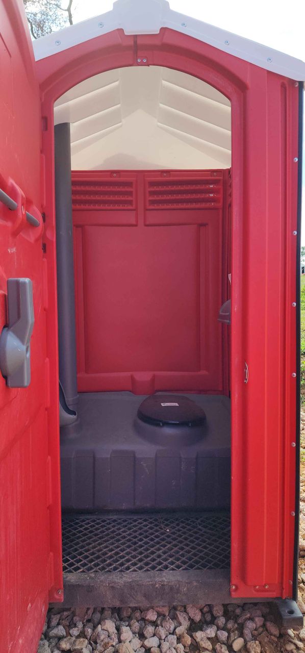 The inside of a red portable toilet with the door open.