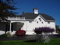 White building with balcony and clock tower, flowers in front, blue sky.