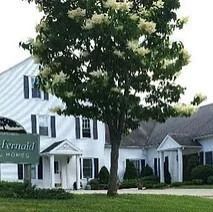 White building with green sign, tree in front.