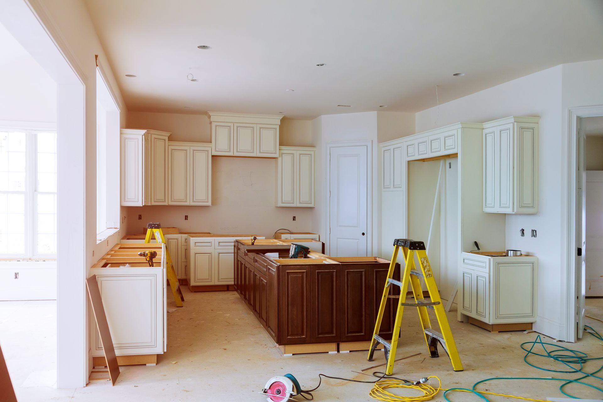A kitchen is being remodeled in a house with a ladder in the middle of the room.