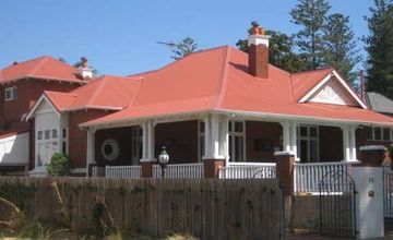 House with a red roof, white trim, and wraparound porch behind a wooden fence and trees