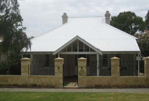 White-roofed house with a front gate and stone fence, surrounded by trees and grass.