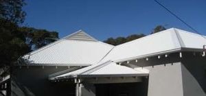 White-roofed buildings with a covered entrance, seen from outside against a blue sky.