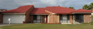Single-story brick house with red roof and a large gray garage, fronted by a lawn