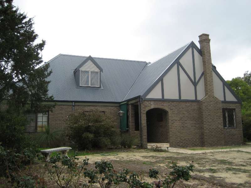 Stone house with gray metal roof, arched entry, and Tudor-style gable in a grassy yard