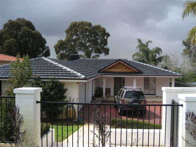 Suburban house with black roof and front gate, parked SUV in driveway, under cloudy sky