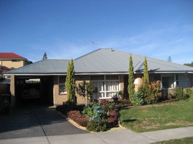 Single-story suburban house with gray roof, driveway, front garden, and blue sky
