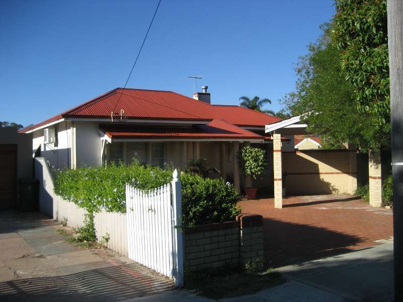 Single-story house with red roof, white fence, and a brick driveway in sunny daylight