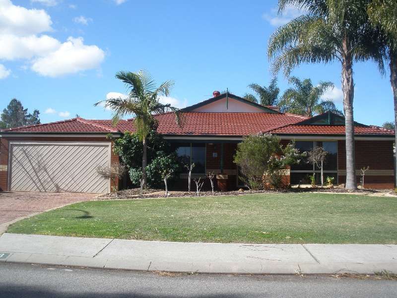 Suburban house with red roof, garage, palm trees, and a green lawn under a blue sky