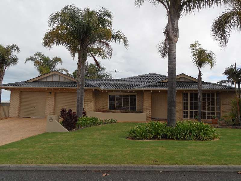 Single-story beige house with a front lawn, palm trees, and a driveway under an overcast sky