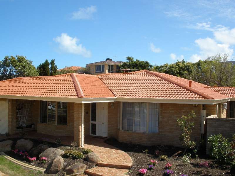 Single-story brick house with terracotta roof, front porch, and landscaped garden under a blue sky