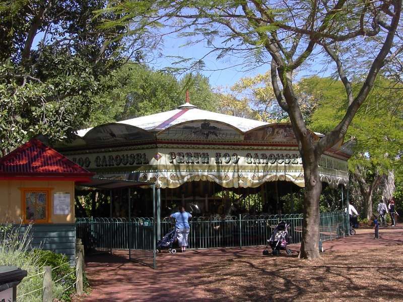Outdoor carousel pavilion with a white roof, trees, and a few people sitting nearby