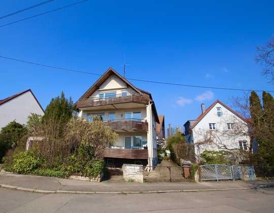 Straßenansicht von zwei Häusern, darunter ein braunes Haus im Chalet-Stil mit Balkonen unter blauem Himmel
