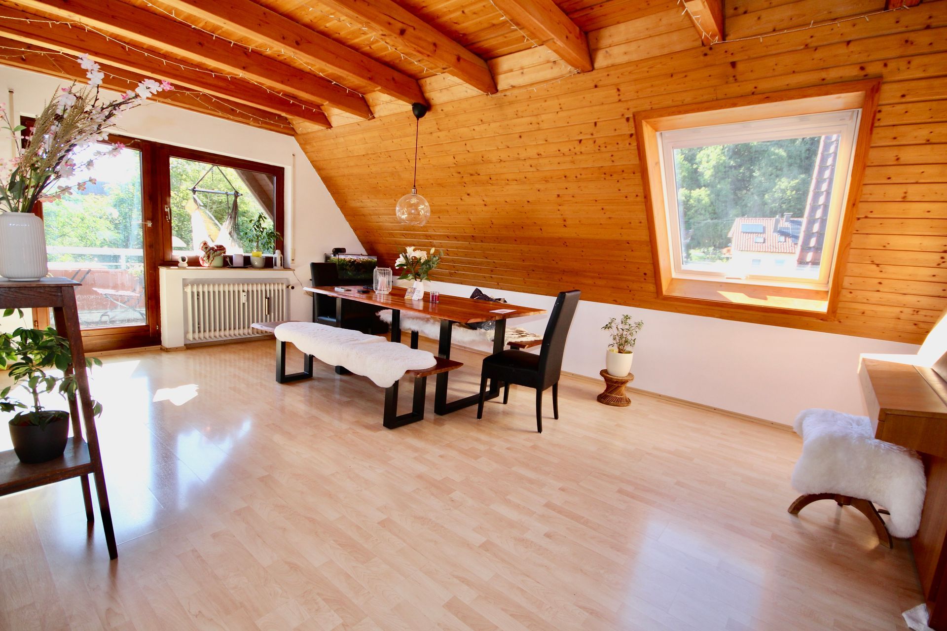 Helles, holzgetäfeltes Esszimmer mit großen Fenstern, weißem Tisch, schwarzen Stühlen und einer Bank.