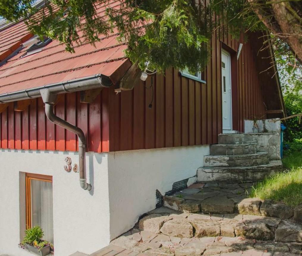 Rotes Holzhaus mit weißer unterer Wand und Steinstufen neben einem grasbewachsenen Hang
