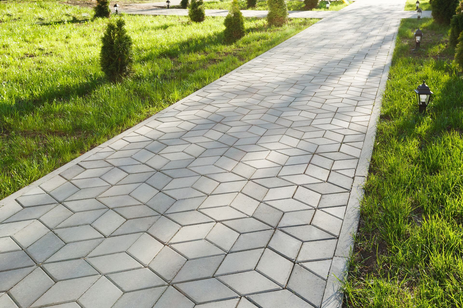 Colorful brick walkway beside a neatly trimmed green hedge in sunlight
