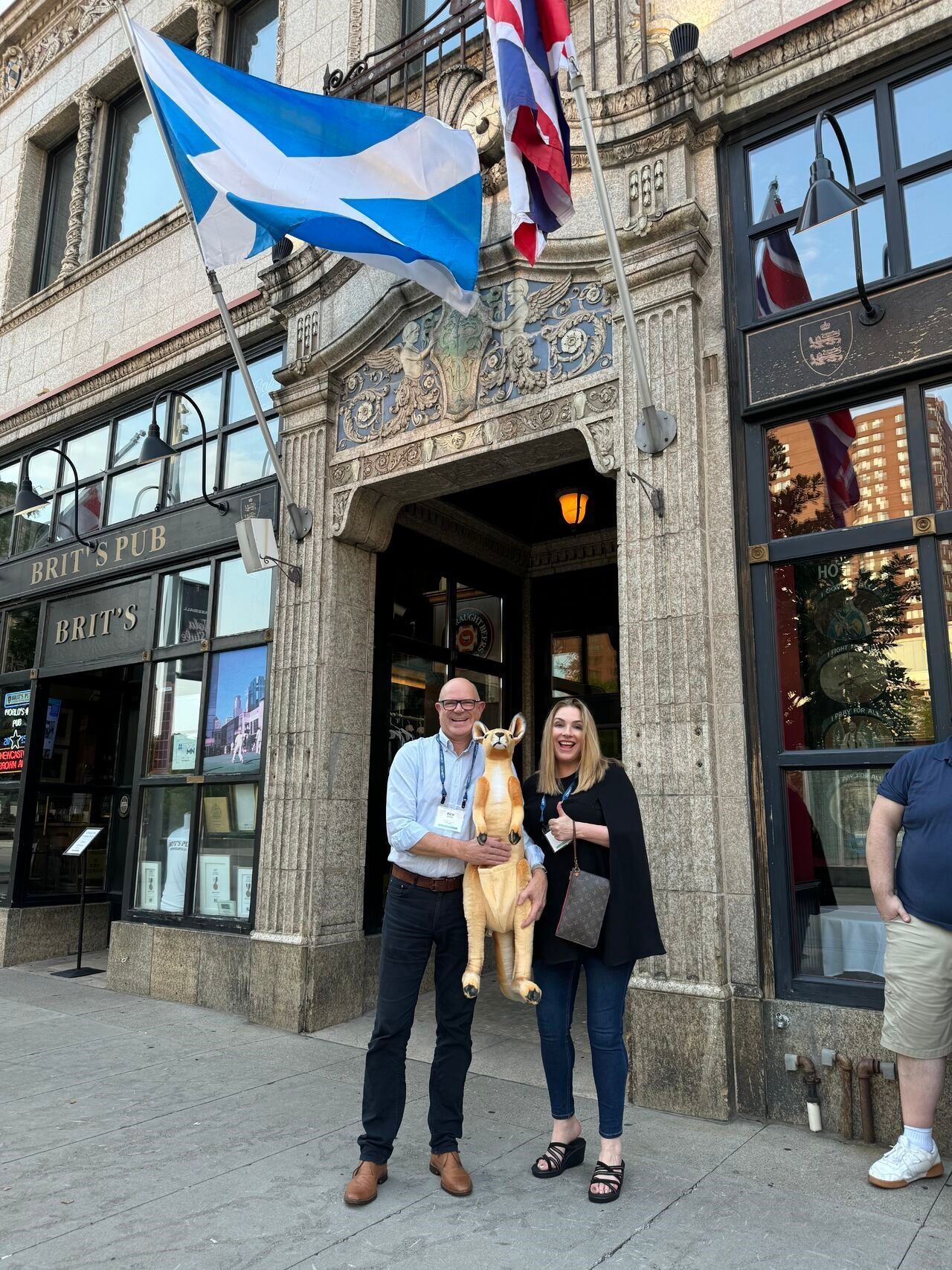 A man and woman holding a kangaroo statue outside an ornate stone building with a Scottish flag.