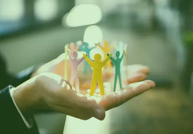 Hands cupping a colorful ring of interconnected paper cutout figures, symbolizing community, teamwork, and support.