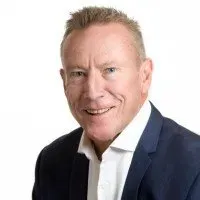 A man wearing a dark blue suit jacket and a white button-down shirt against a white background.