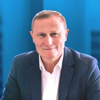 A professional portrait of a man in a navy blue blazer and white shirt against a bright blue background.