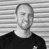 Headshot of a smiling person in a dark shirt standing in front of a corrugated metal wall.