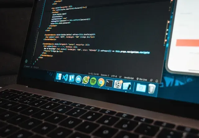A MacBook Pro displaying code in an editor with a dock of application icons visible at the bottom of the screen.