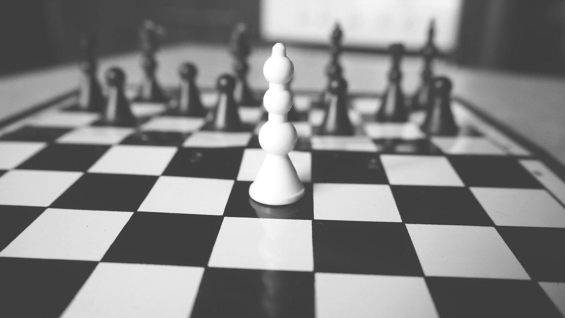 A single white chess piece stands in the center of a black-and-white checkered board surrounded by dark pieces.